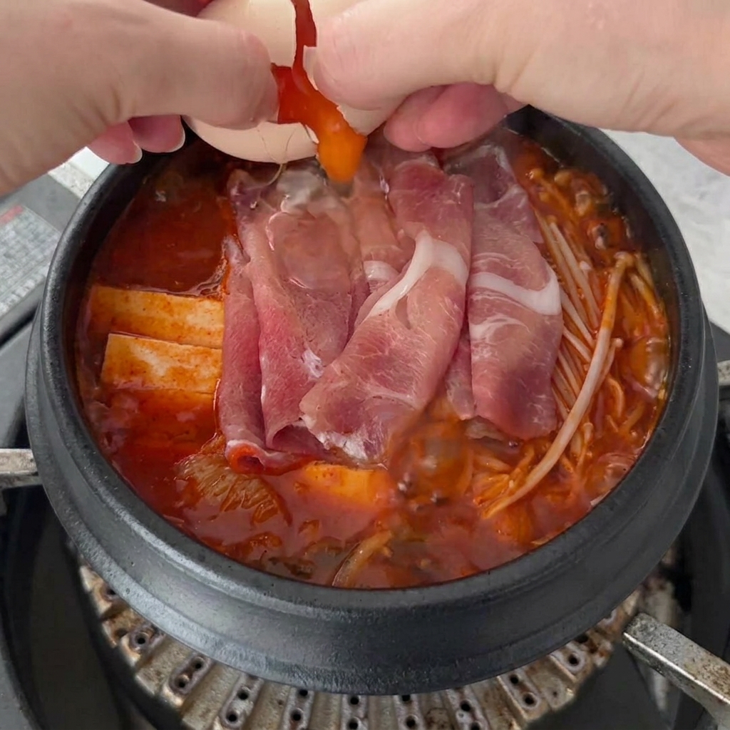 Deux œufs frais cassés sur la surface bouillonnante du Kimchi Jjigae, avec le bouillon et les ingrédients visibles en dessous.