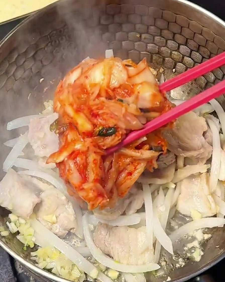Kimchi assaisonné rouge mélangé au porc et aux oignons dans la casserole.