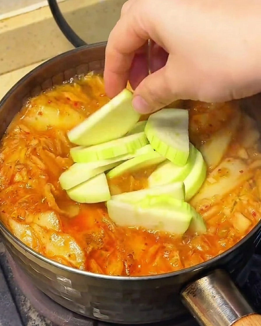 Légumes, dont des tranches de chayote, pousses de soja et champignons enoki, ajoutés dans la soupe frémissante.