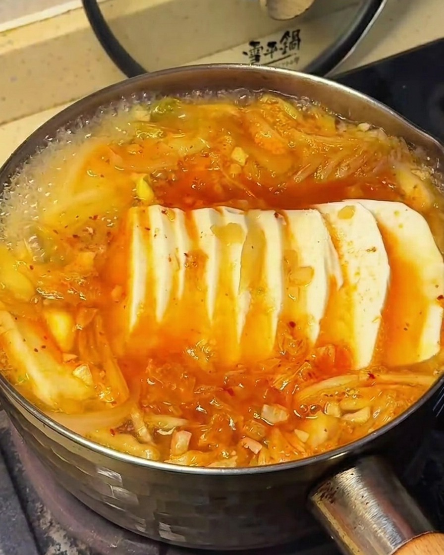 La surface de la soupe au kimchi avec tofu, montrant lassaisonnement saupoudré sur les ingrédients.