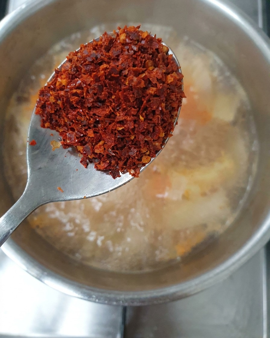 Cuillerée de flocons de piment rouges tenue au-dessus du ragoût.