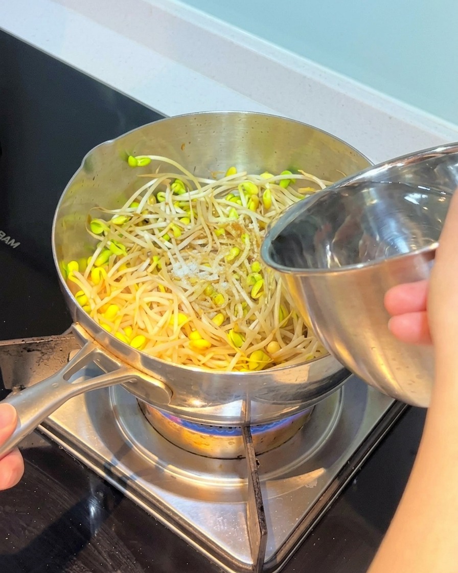 Eau versée depuis un bol en inox dans la casserole contenant les ingrédients.