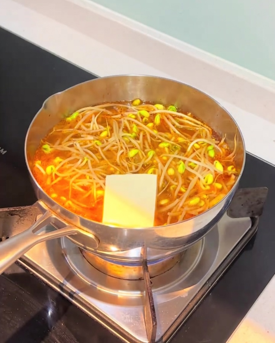 Tranches de tofu blanc et gâteaux de poisson ajoutés dans le bouillon orange frémissant.