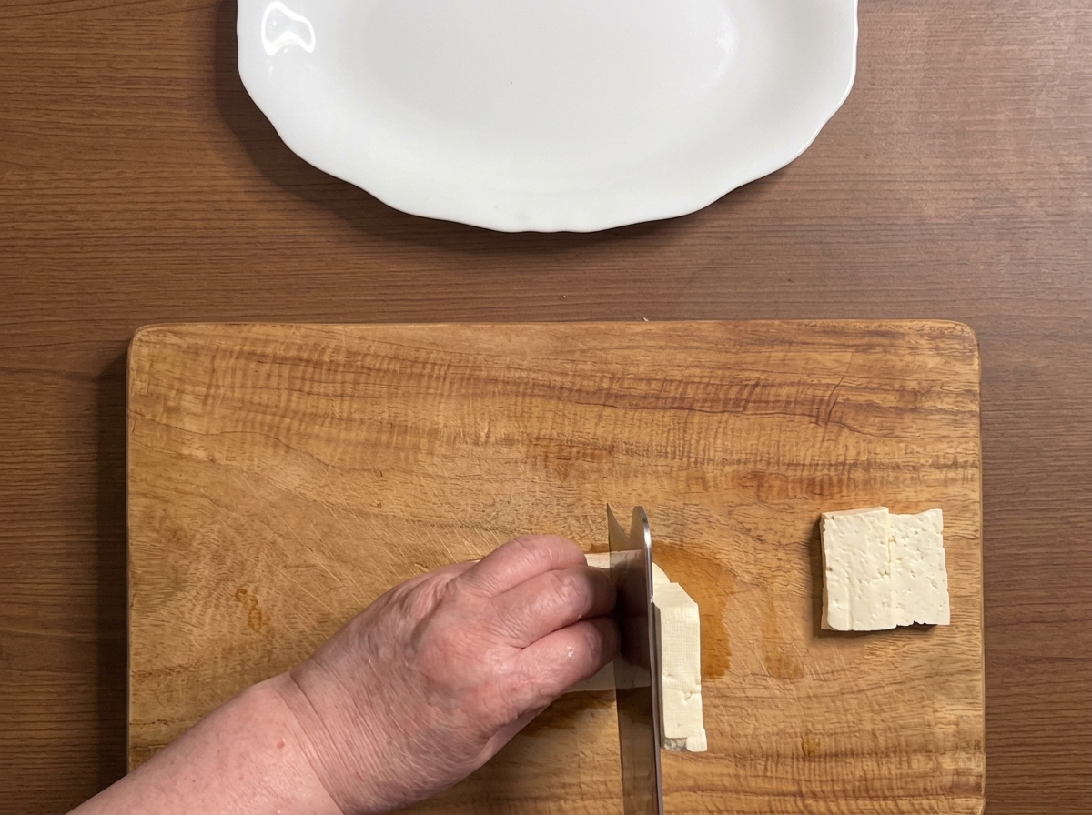 Bloc de tofu coupé en tranches épaisses et nettes sur une planche à découper en bois.