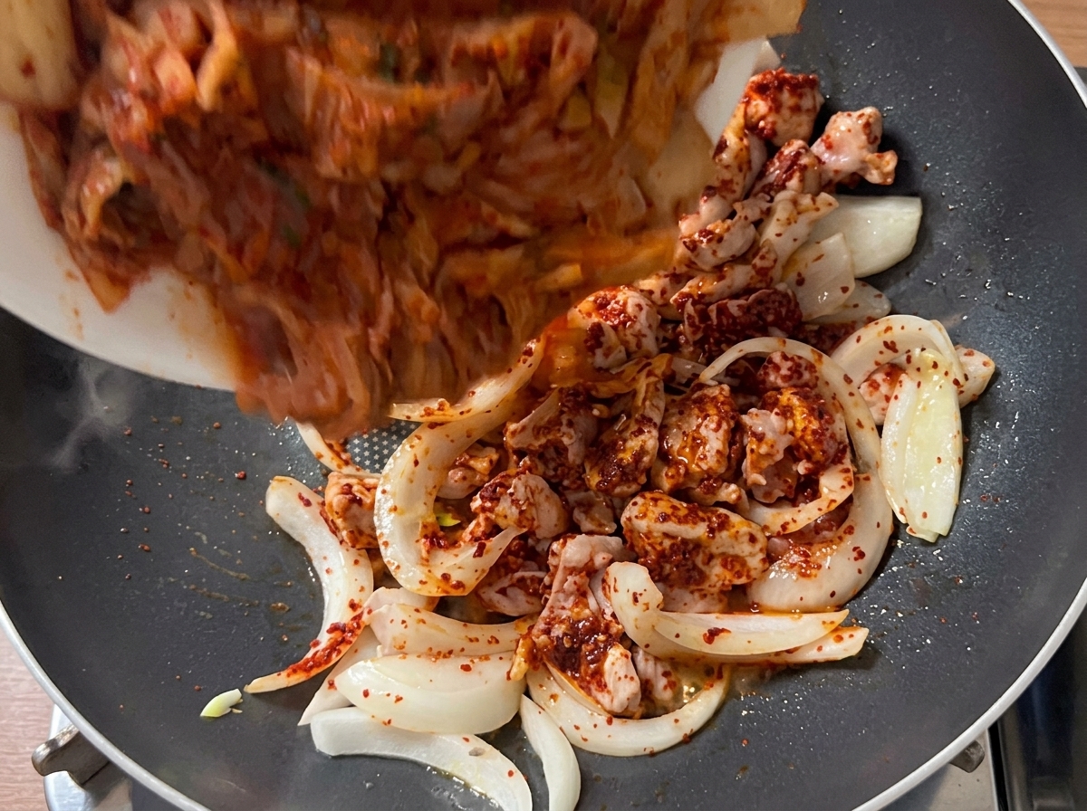 Morceaux de kimchi de la taille dune bouchée versés dans la poêle avec le mélange de porc et doignon dorés.