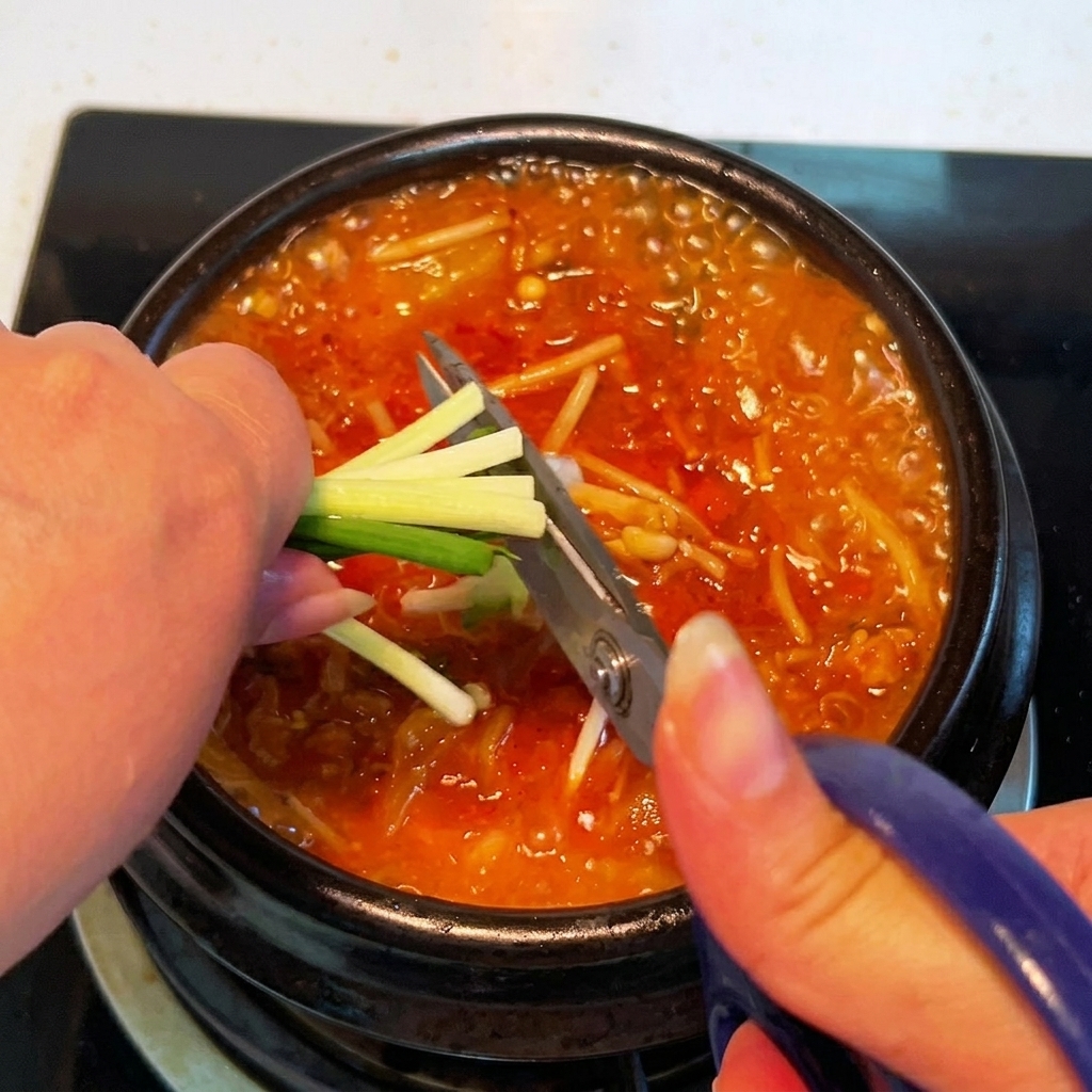 Oignons verts frais coupés directement au-dessus du pot de ragoût de kimchi avec des ciseaux de cuisine.