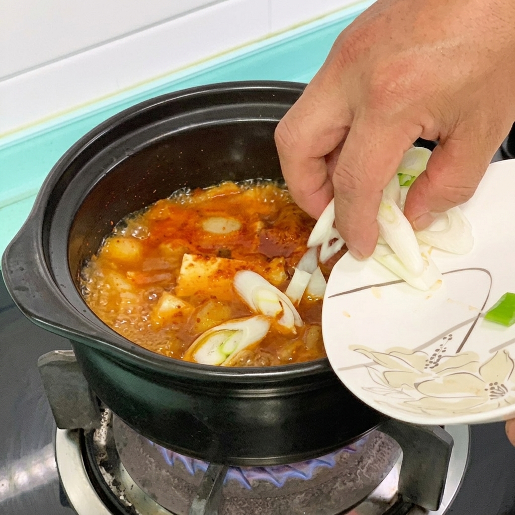 Piment vert et oignon vert ajoutés dans une casserole de ragoût de tofu rouge.