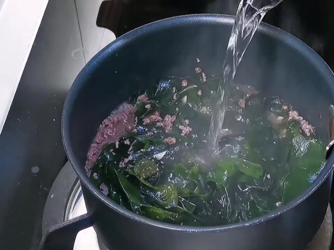 Eau fraîche versée dans la marmite sur le mélange de bœuf et wakame.