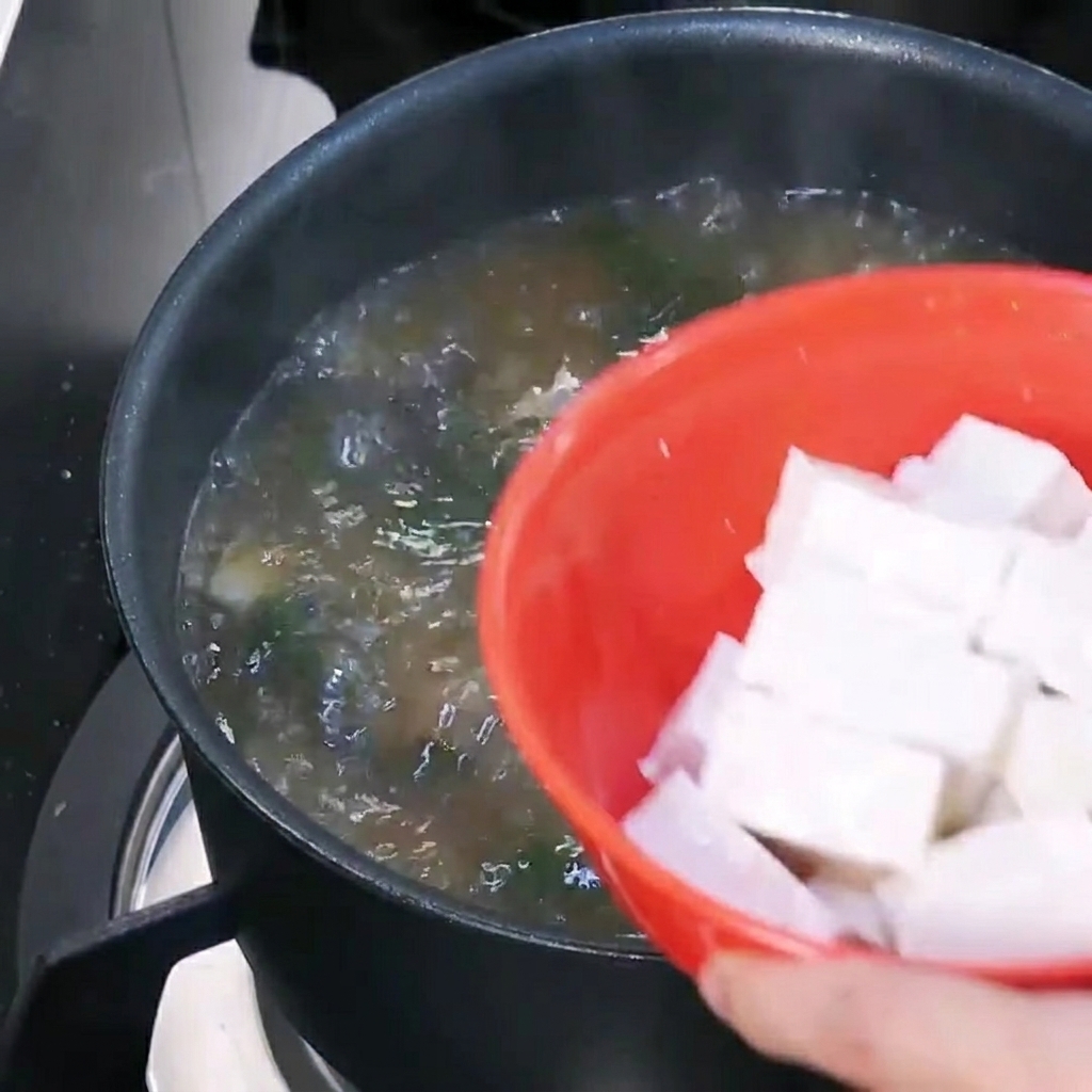 Dés de tofu ajoutés dans la soupe coréenne bouillante.