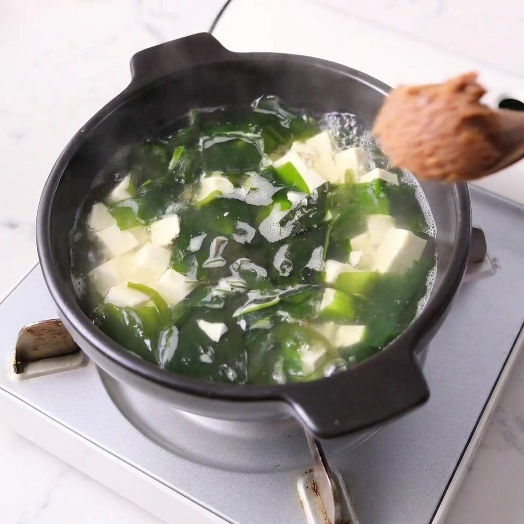 Une cuillère de pâte miso mélangée dans la casserole avec le tofu et le wakame.