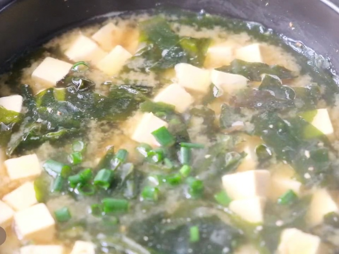 Gros plan sur une casserole de soupe miso avec tofu, algues et oignons verts frais sur le dessus.