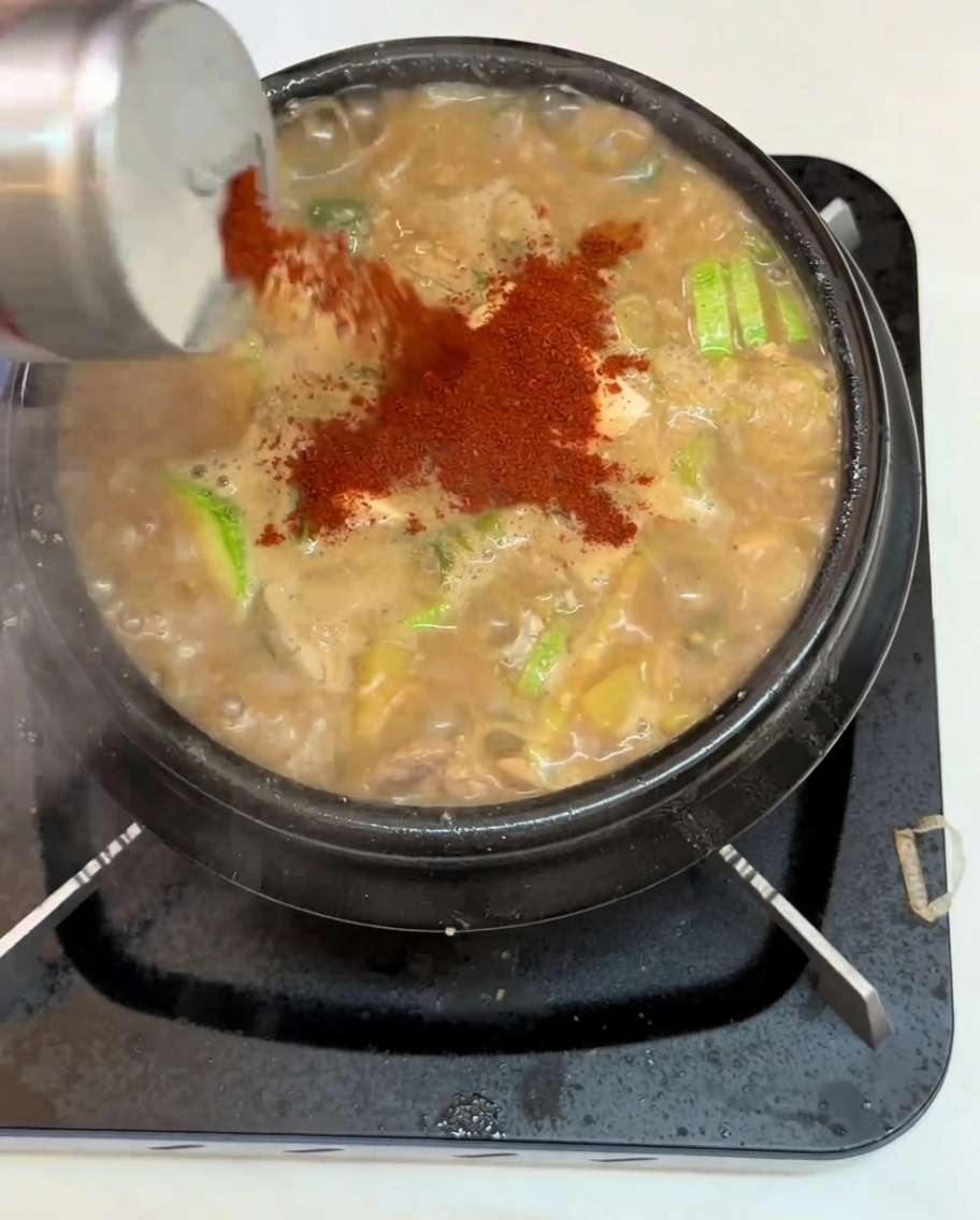 Gros plan sur de la poudre de piment saupoudrée sur un pot de ragoût de pâte de soja bouillonnant contenant du tofu et des légumes.