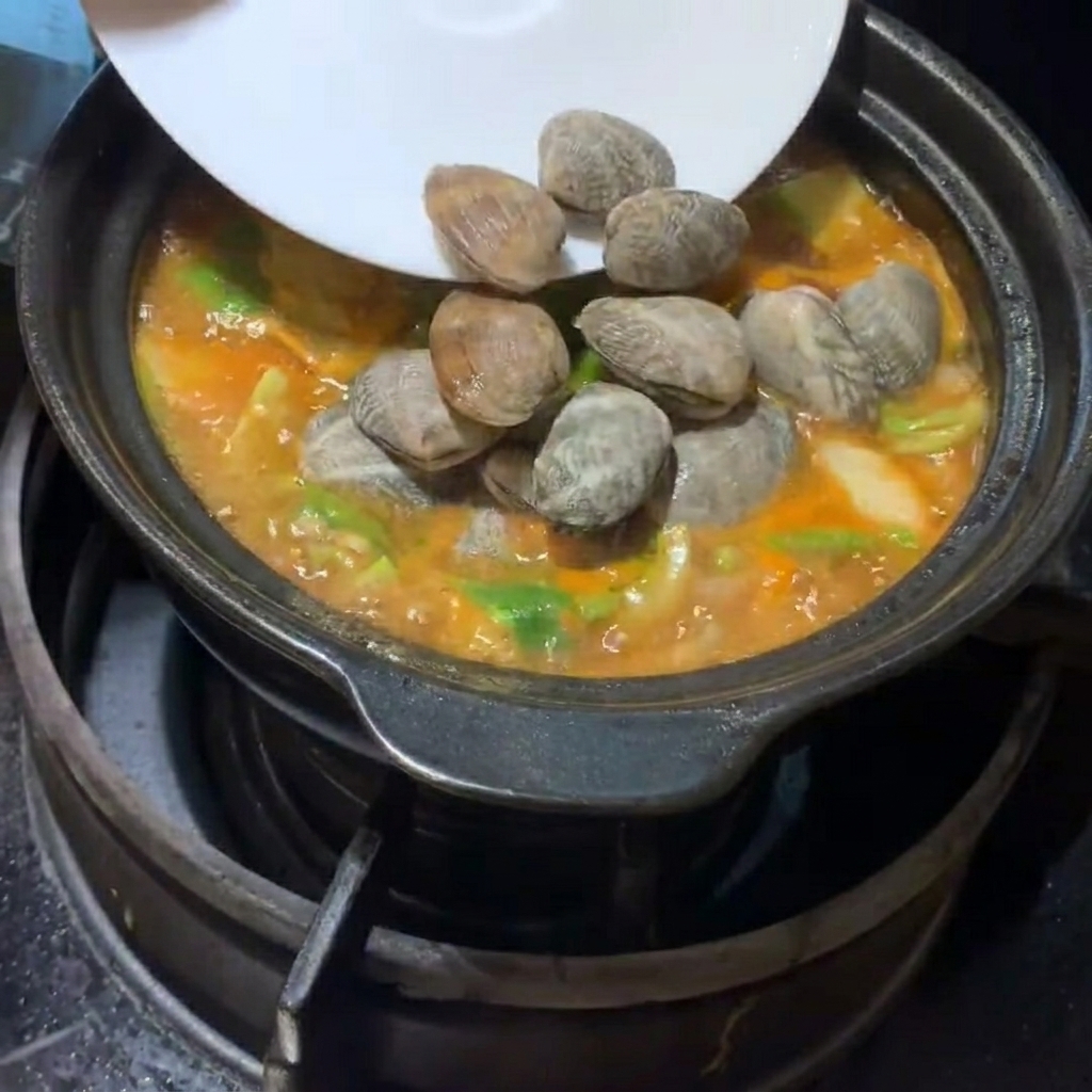 Palourdes fraîches et dés de tofu déposés délicatement dans le ragoût frémissant.