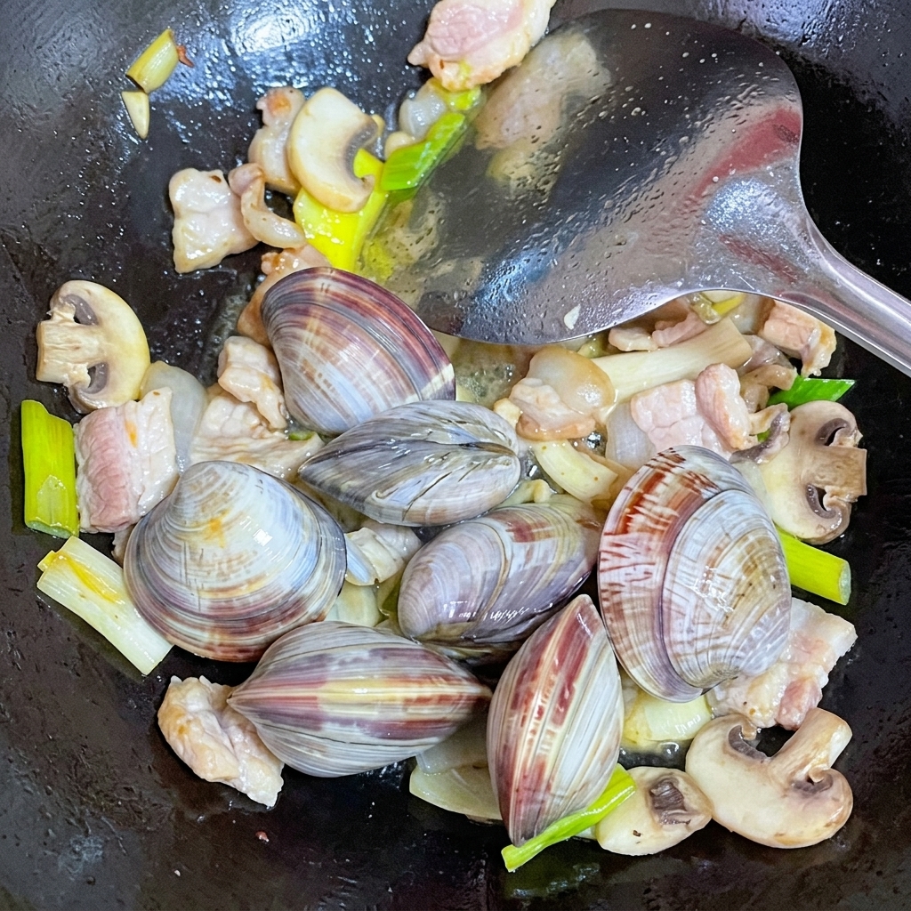 Palourdes fraîchement nettoyées ajoutées dans un wok avec le porc et les champignons.