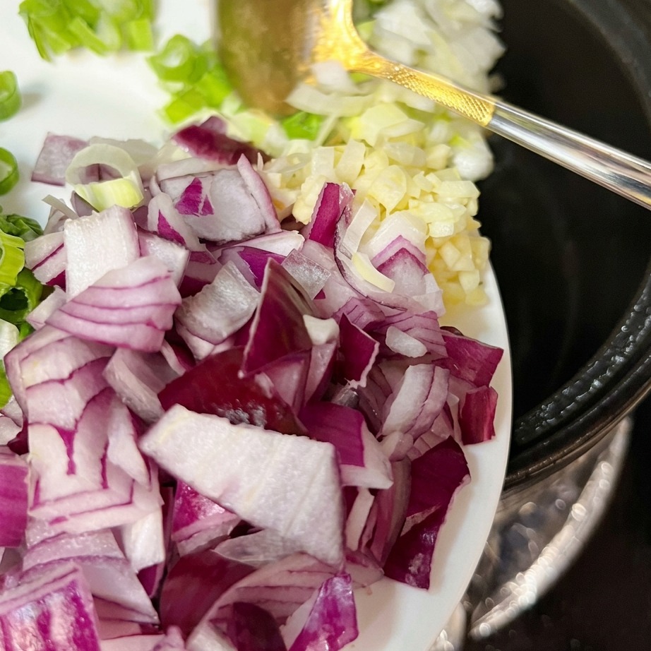 Oignons verts frais, ail et oignon rouge ajoutés au porc sauté dans le pot.