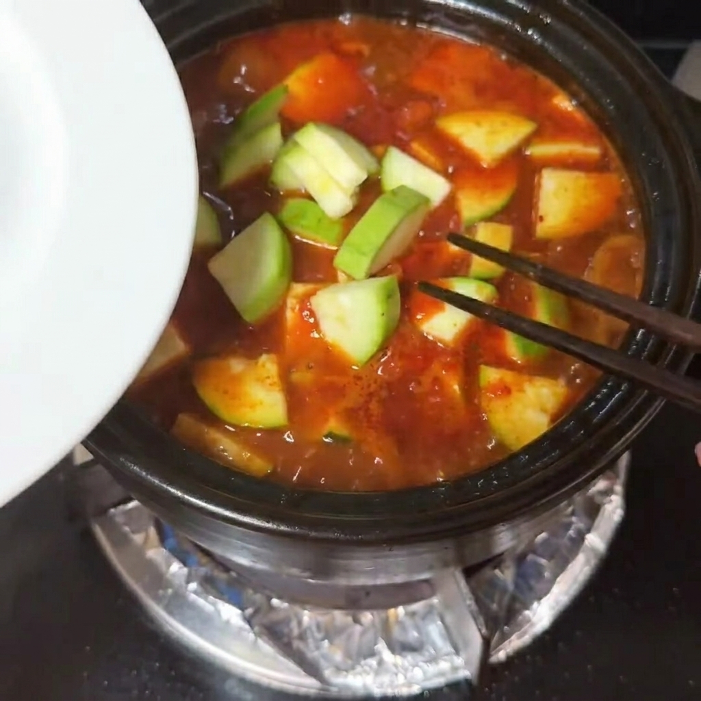 Tranches de courgette et cubes de tofu soyeux placés dans une soupe rouge bouillonnante.