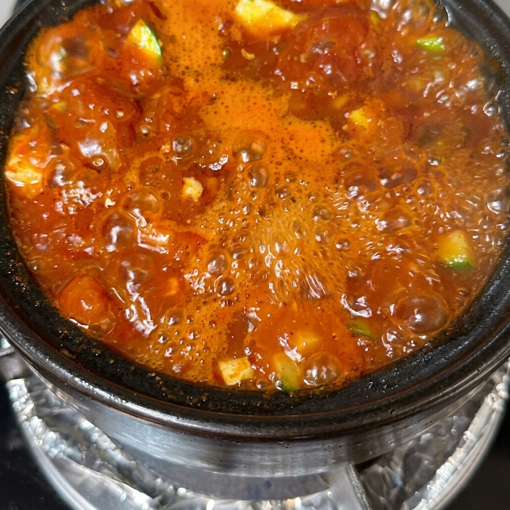 Un pot de soupe au tofu terminé, garni doignons verts émincés et de piments rouges.