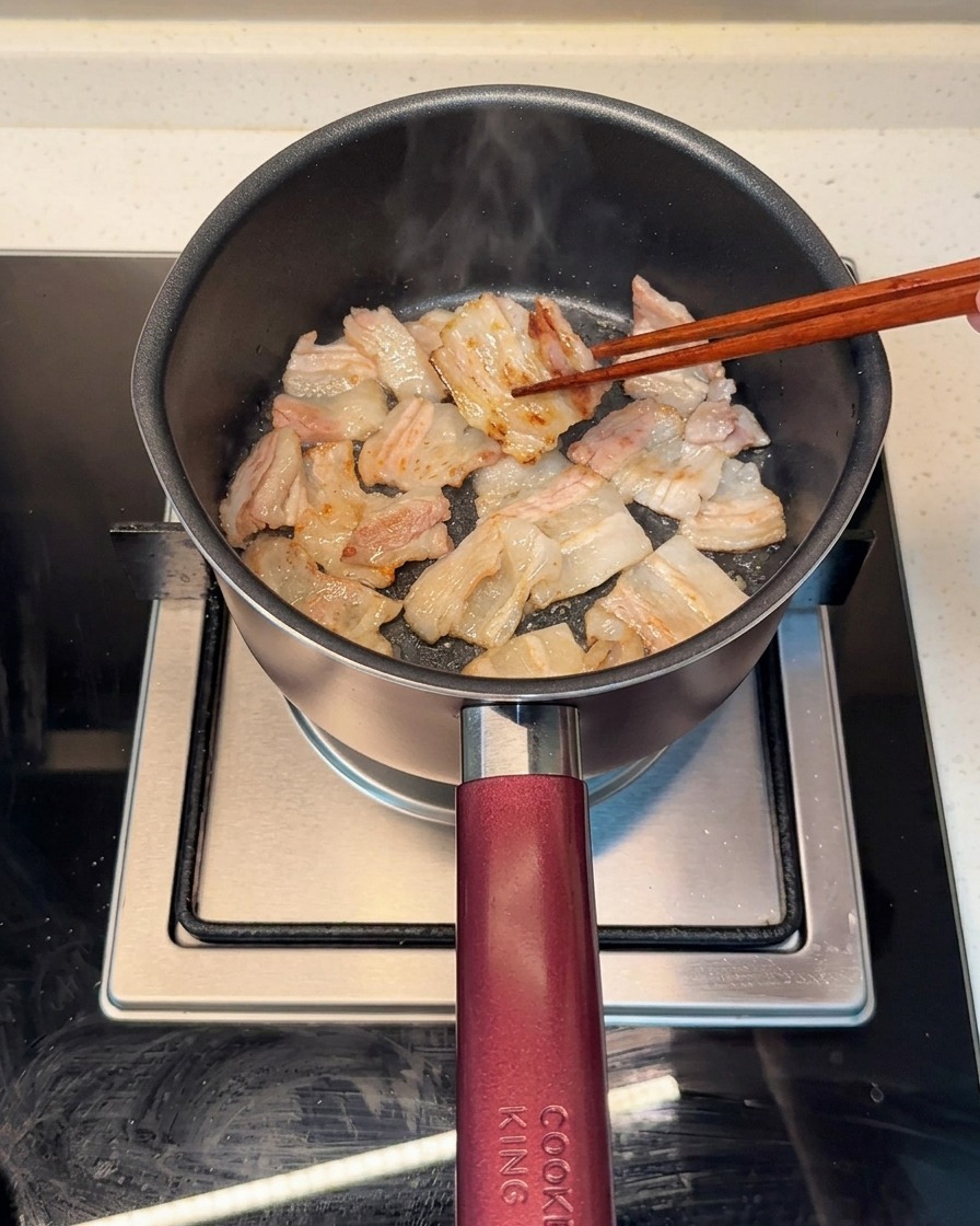 Tranches de poitrine de porc qui dorent uniformément dans une marmite, avec la graisse fondue visible.