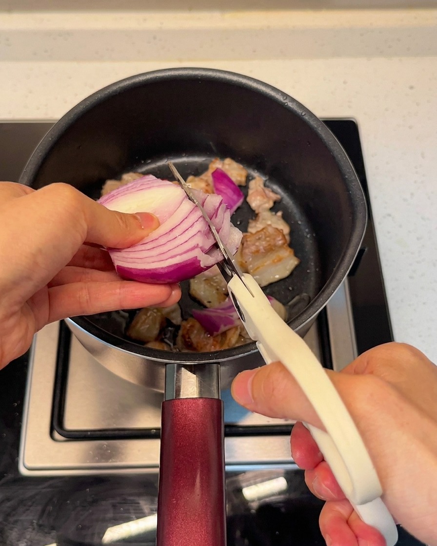 Couper un oignon rouge frais directement dans la marmite avec le porc à laide de ciseaux de cuisine.