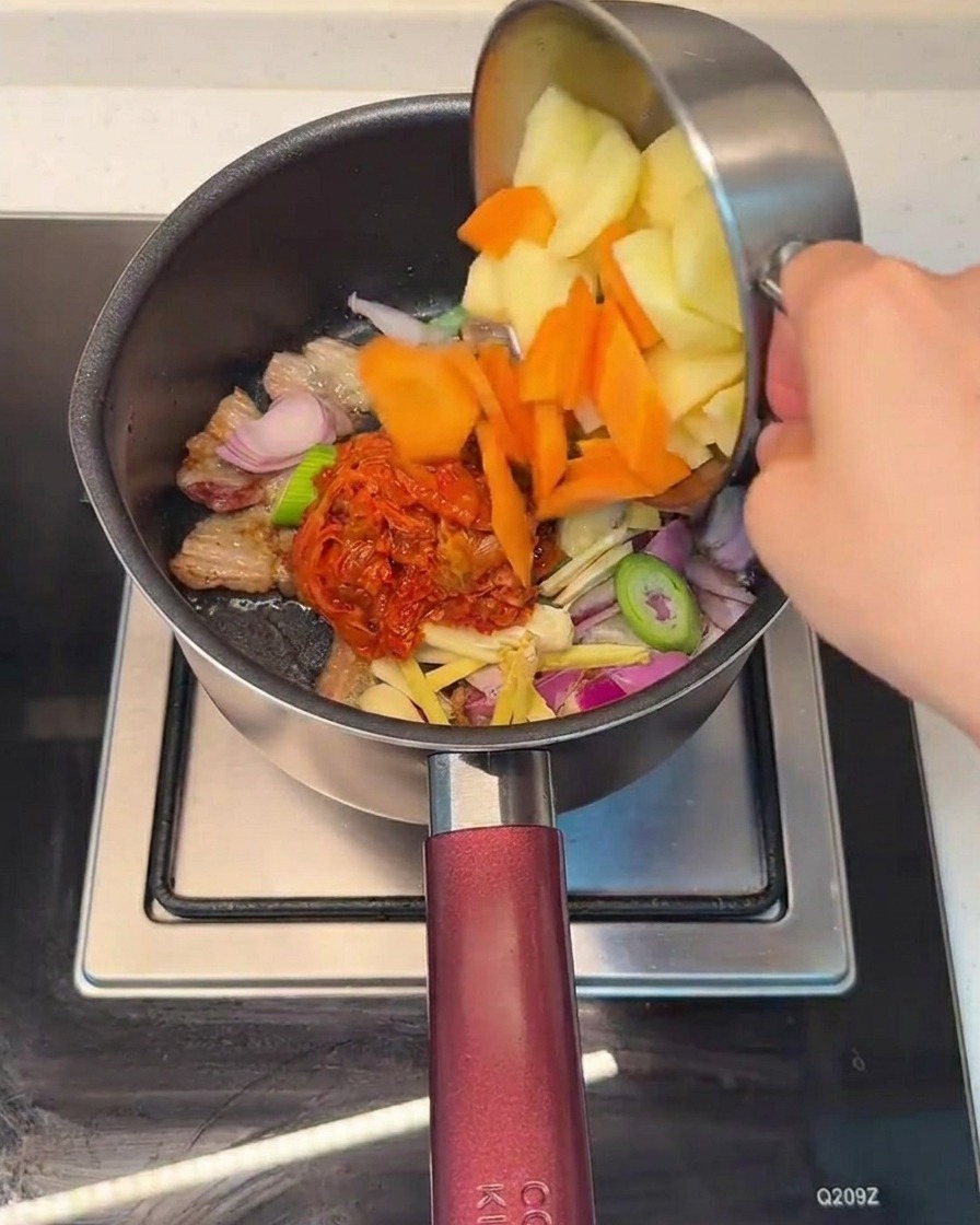 Ajout de carottes et de pommes de terre coupées dans la marmite contenant le mélange de porc et de kimchi.