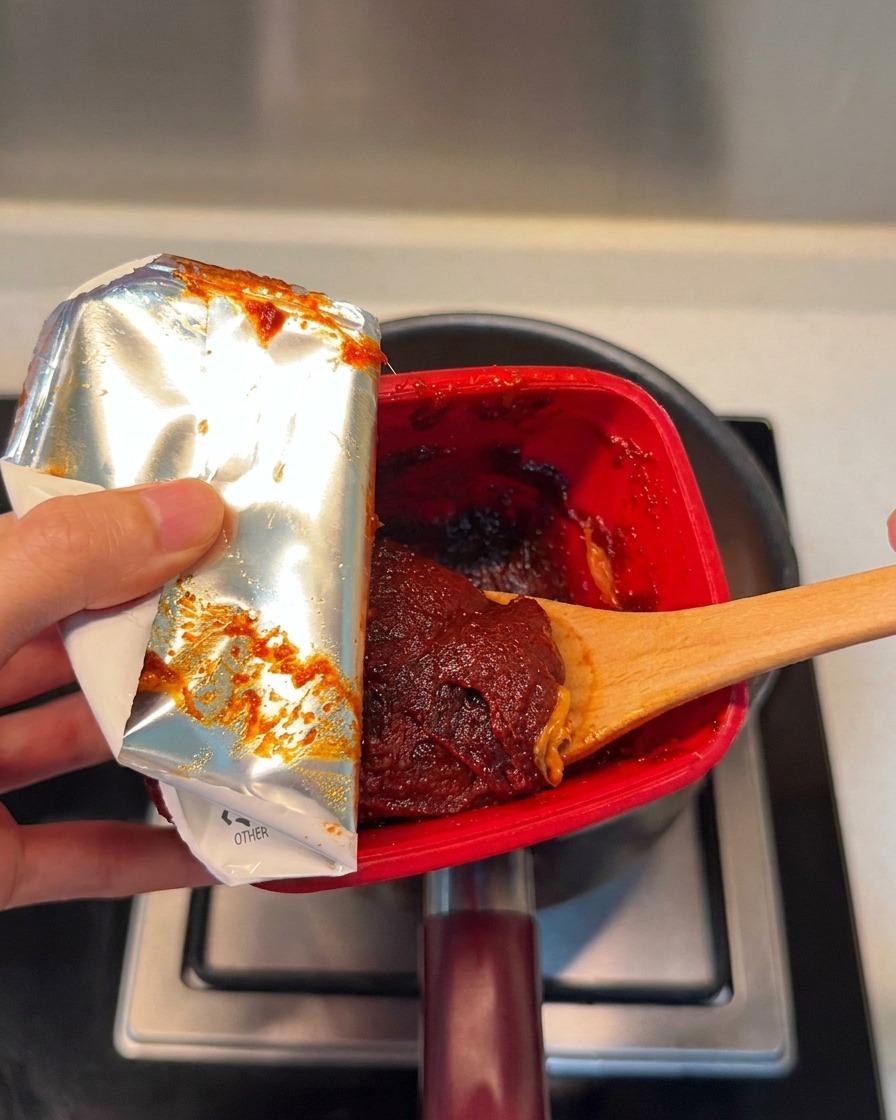Une cuillerée de pâte de piment coréenne rouge et riche ajoutée dans la marmite.