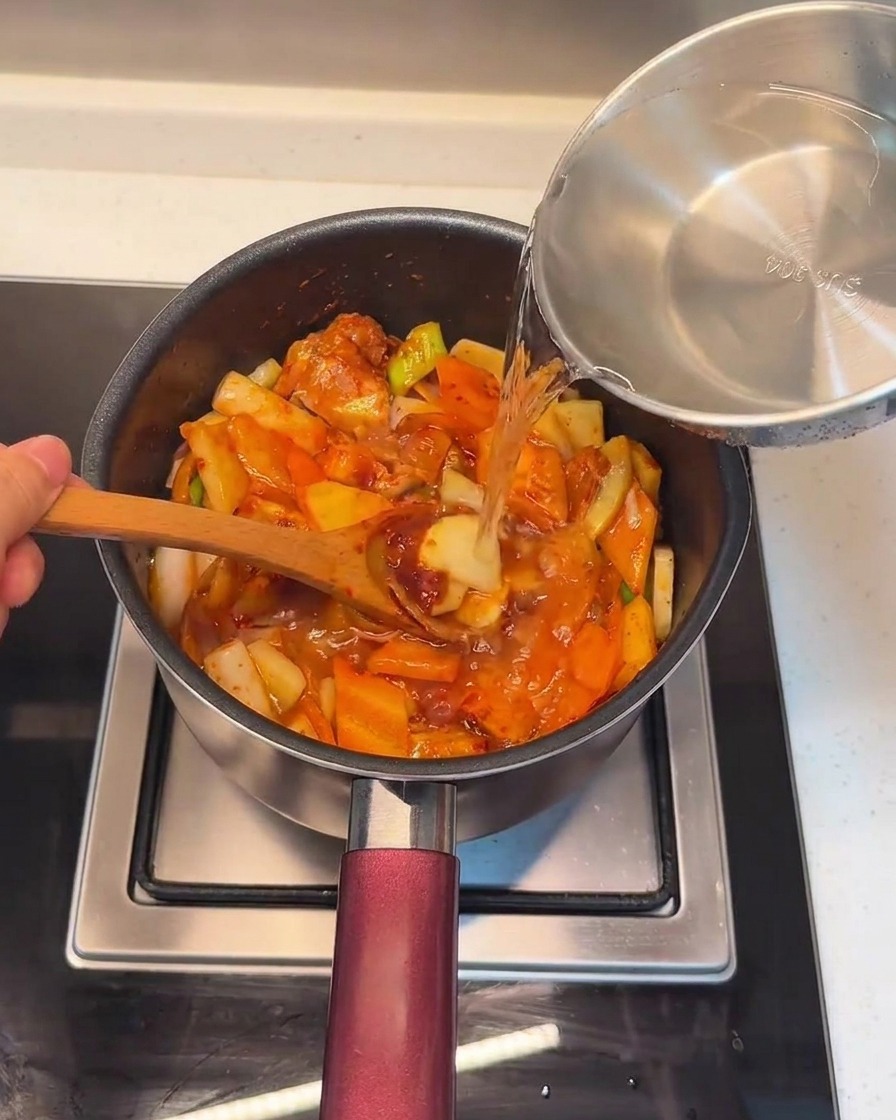 Verser de leau fraîche dans la marmite sur le mélange de porc et de légumes.