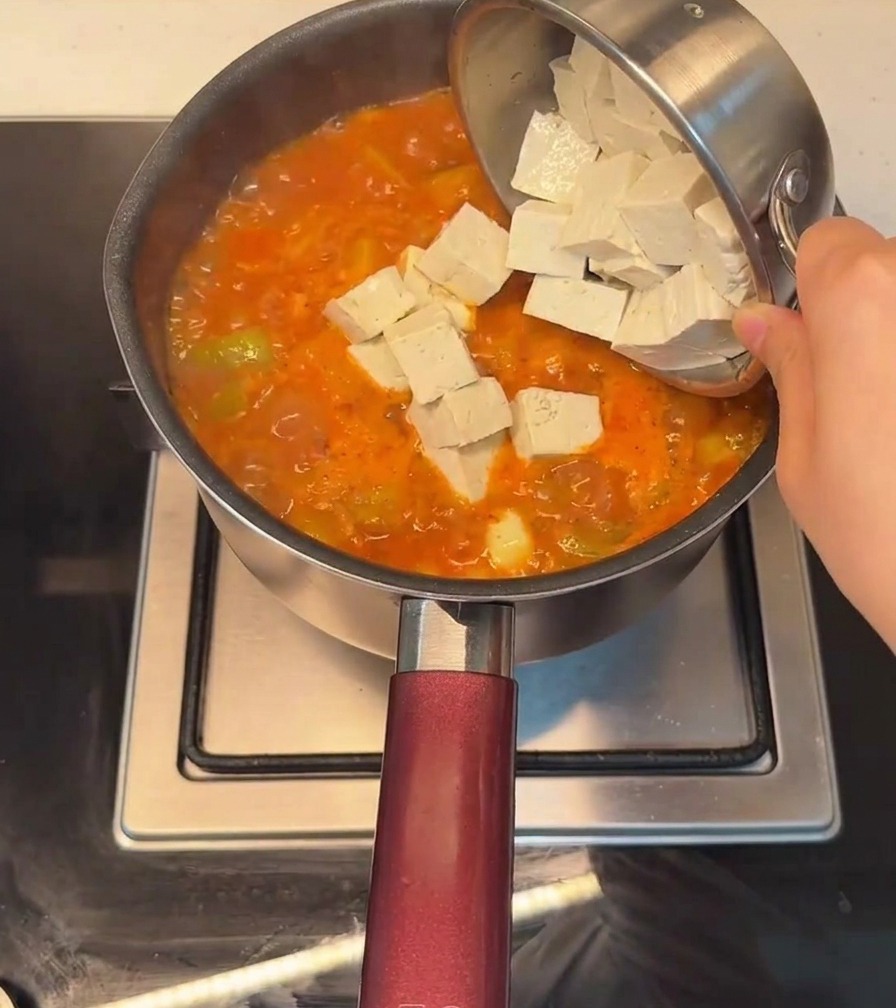 Du tofu en dés ajouté dans une marmite de ragoût épicé bouillonnant.