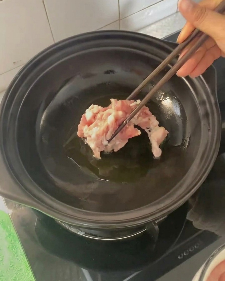 Tranches de poitrine de porc ajoutées dans la cocotte chaude à laide de baguettes.