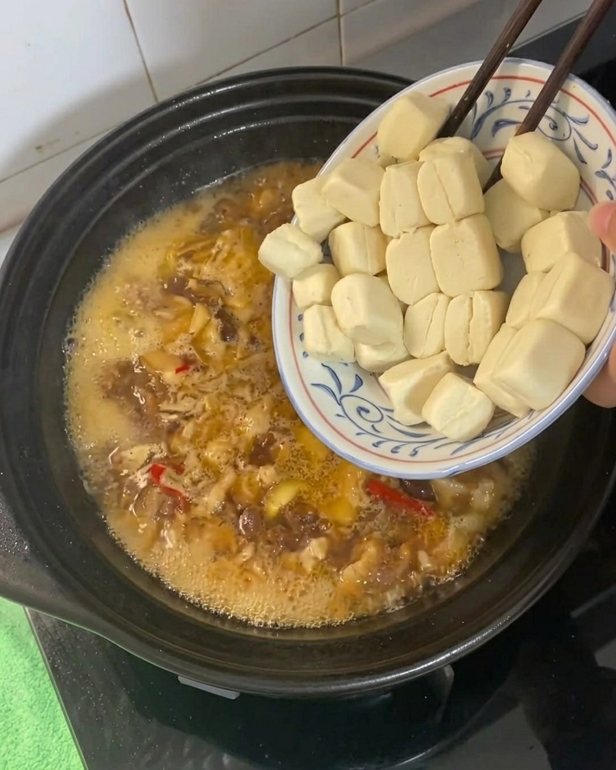 Petits cubes de tofu ajoutés au liquide de braisage bouillonnant dans une cocotte.