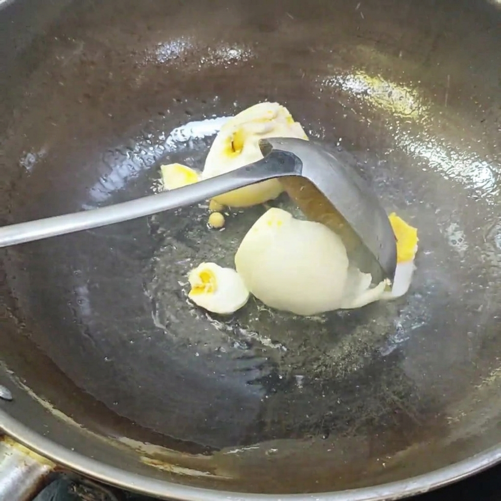 Une louche brisant des œufs de cane salés dans un wok.