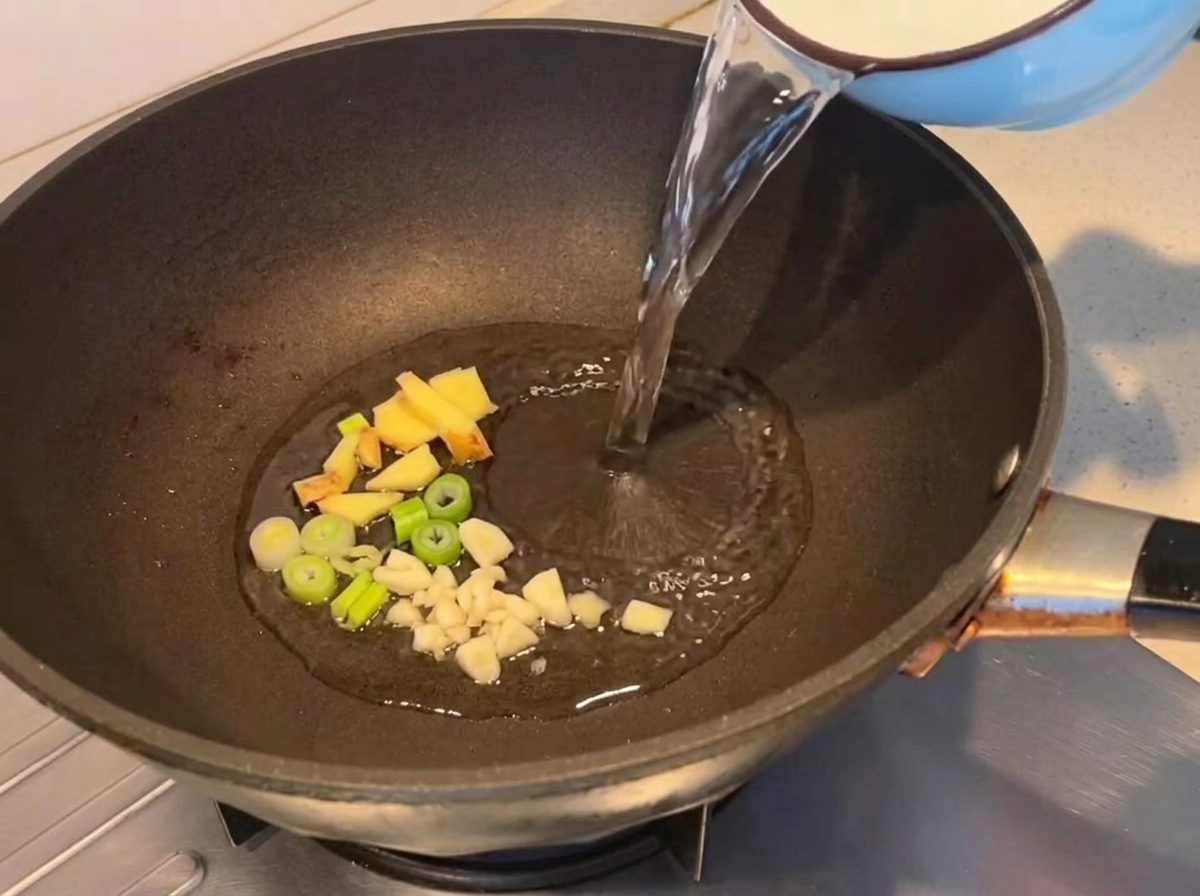 De leau versée dans une poêle avec des aromates sautés.