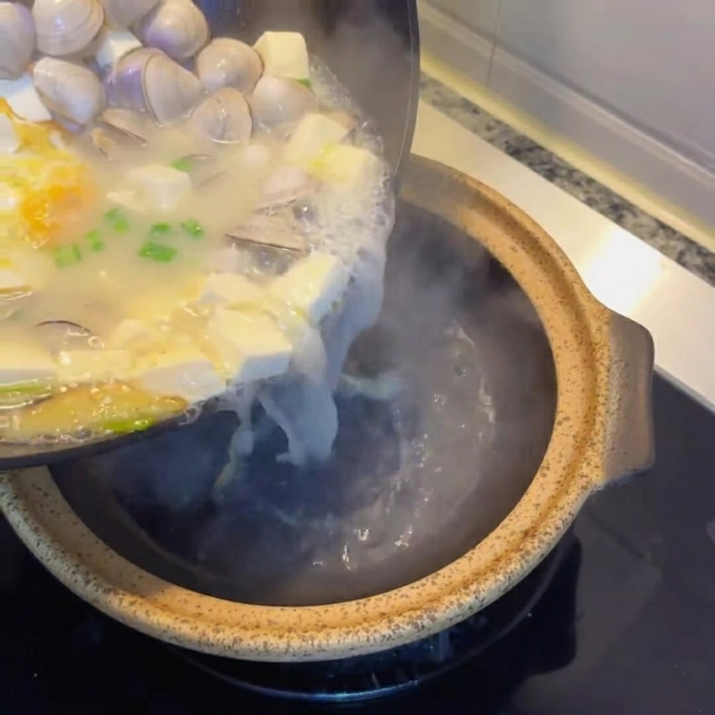 Soupe au tofu et aux palourdes versée dans une marmite de service rustique.