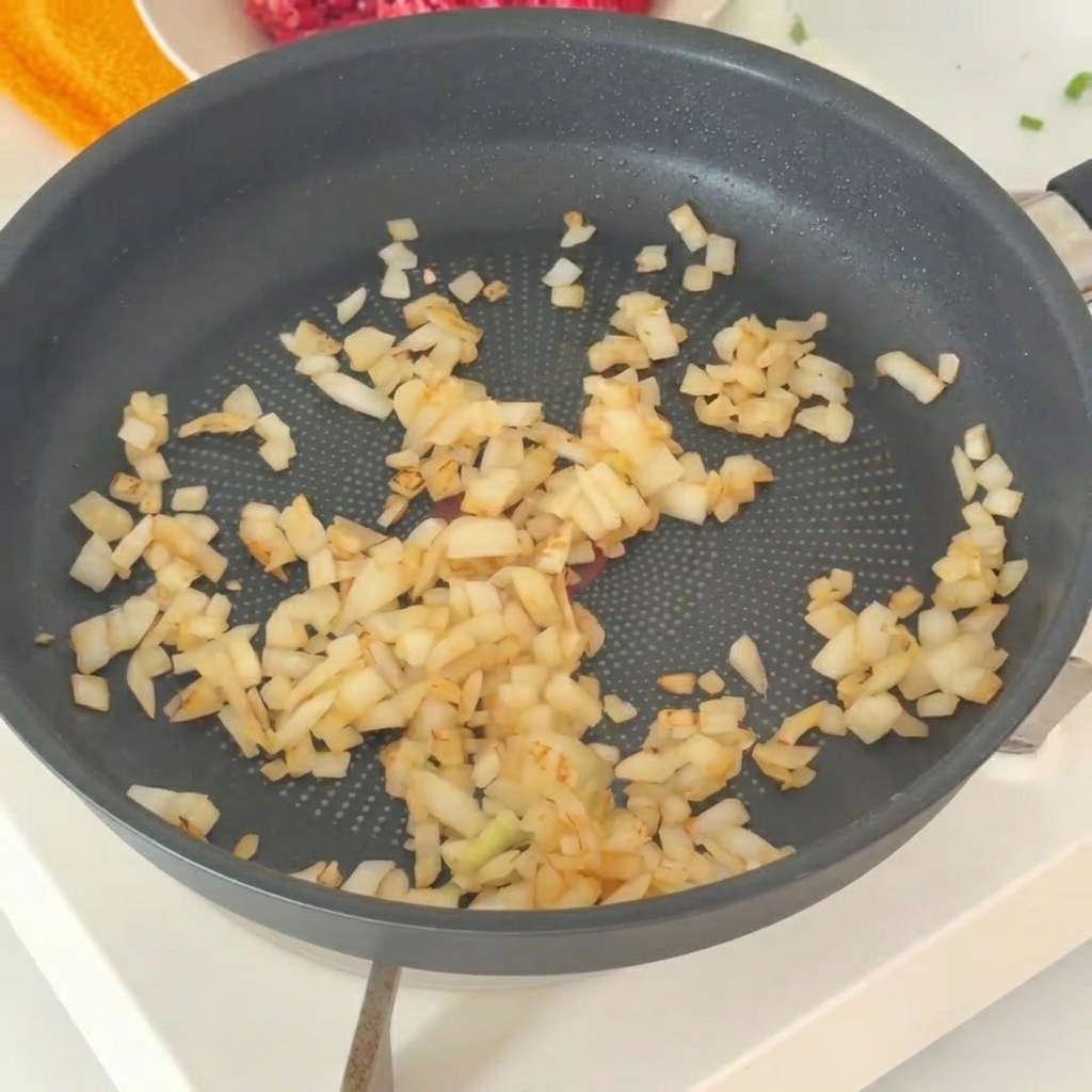 Les oignons sautés transférés dans un bol contenant du bœuf haché frais.