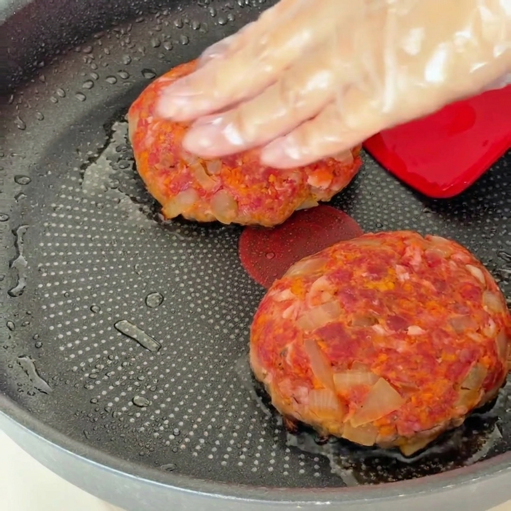Steaks hachés dans une poêle couverts avec un couvercle après avoir été retournés.