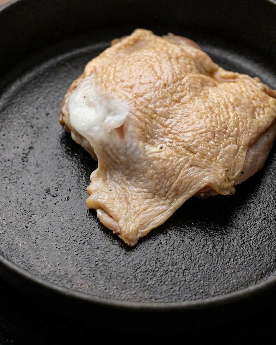 Un morceau de cuisse de poulet mariné qui dore dans une poêle avec du beurre fondu.
