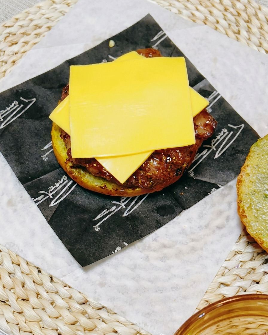 Assemblage du burger avec une tranche de fromage sur le poulet, recouverte de rondelles de concombre.
