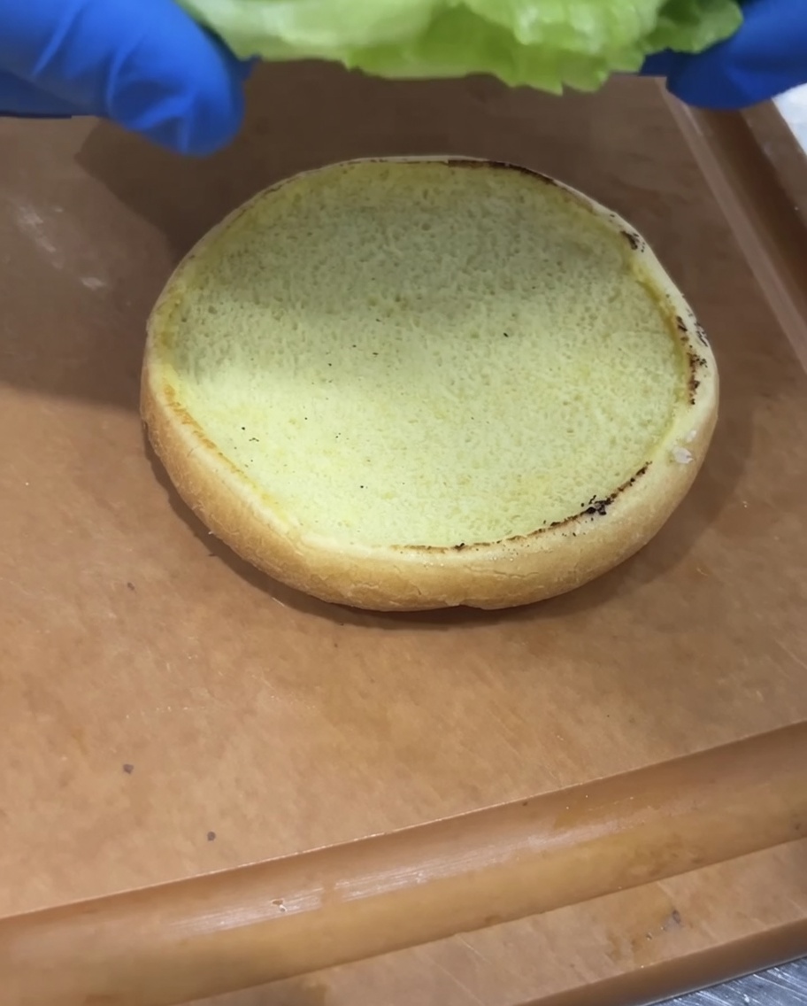 Laitue fraîche et rondelles de tomate placées sur un pain à burger toasté.