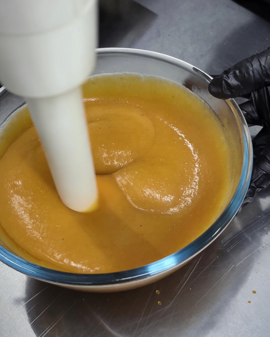 Un mixeur plongeant utilisé pour mixer une sauce épaisse et dorée dans un bol en verre.