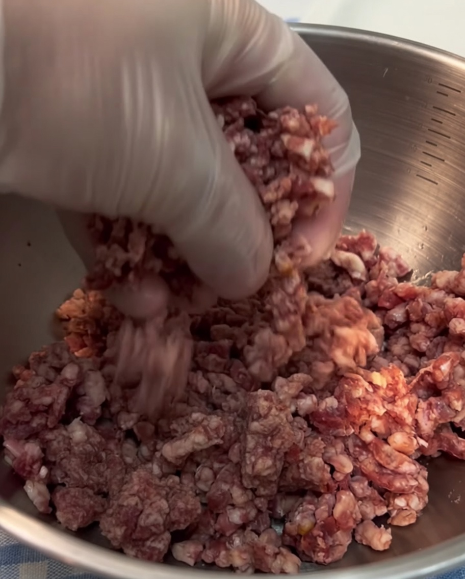 Gros plan sur une main gantée façonnant du bœuf haché frais en une boule compacte.