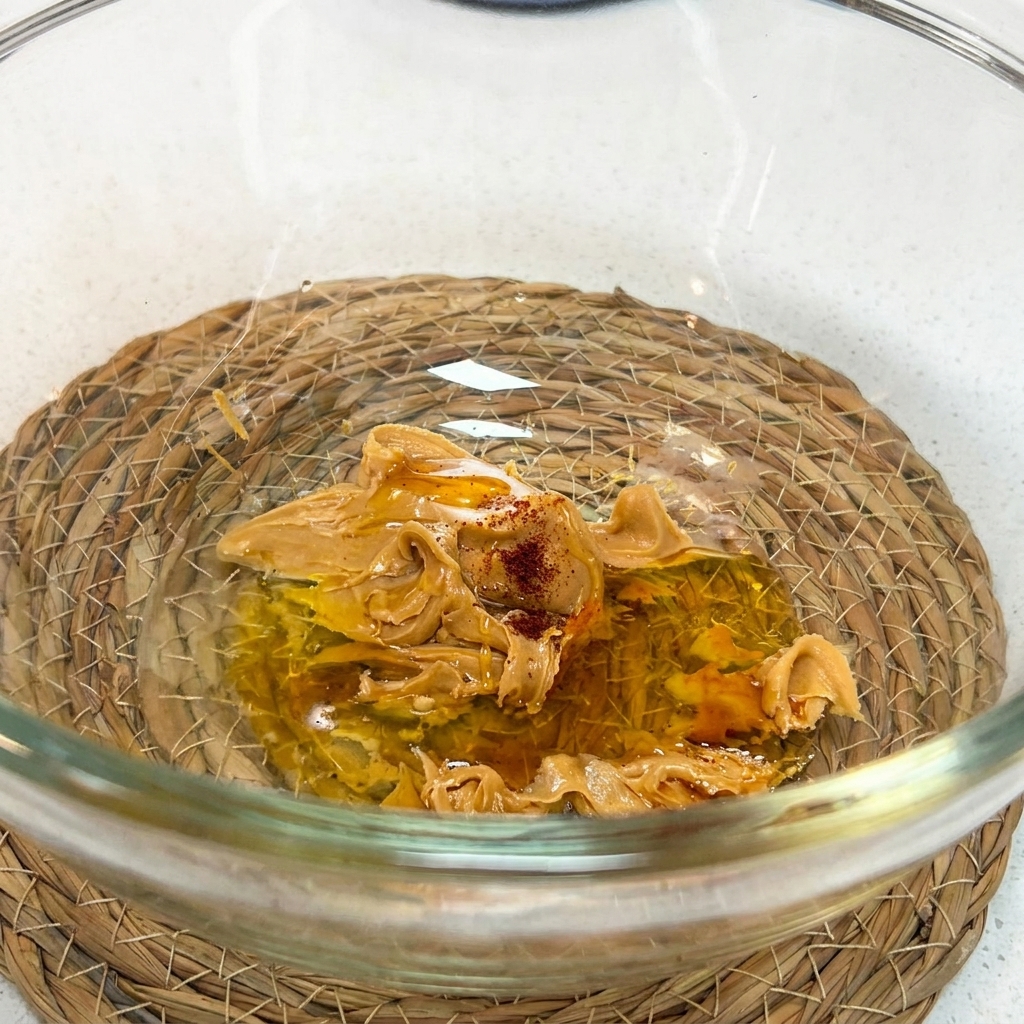 Un fouet mélangeant le beurre de cacahuète, la sauce soja, le miel, le vinaigre, leau et la sauce shacha dans un bol.