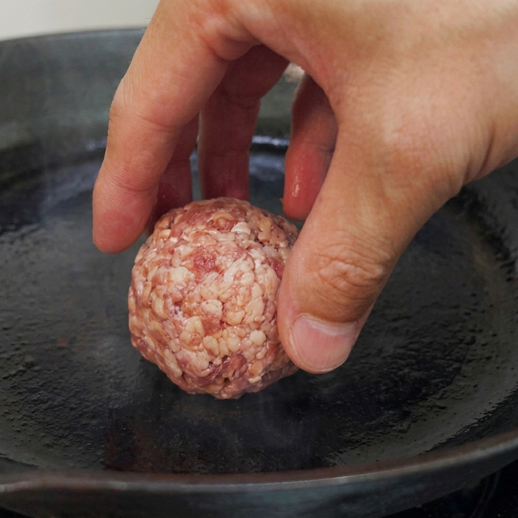 Des boules de bœuf crues déposées dans une poêle à fond plat préchauffée.