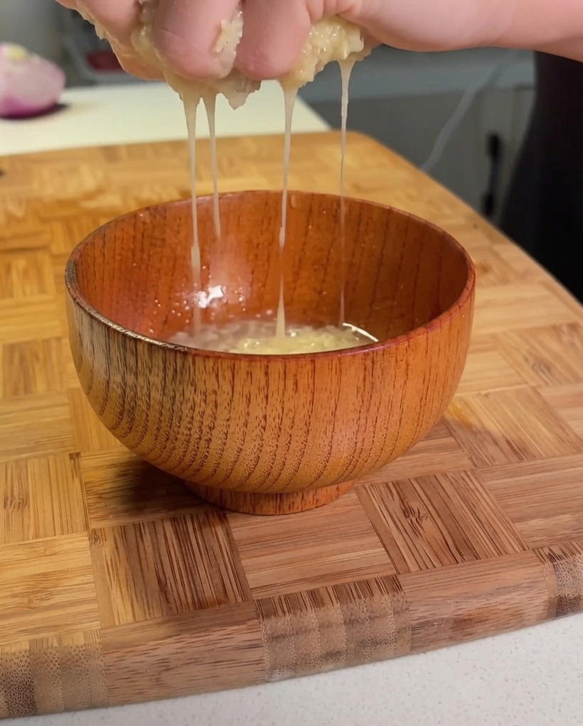 Mains pressant de la pomme de terre râpée au-dessus dun petit bol en bois pour extraire le liquide.