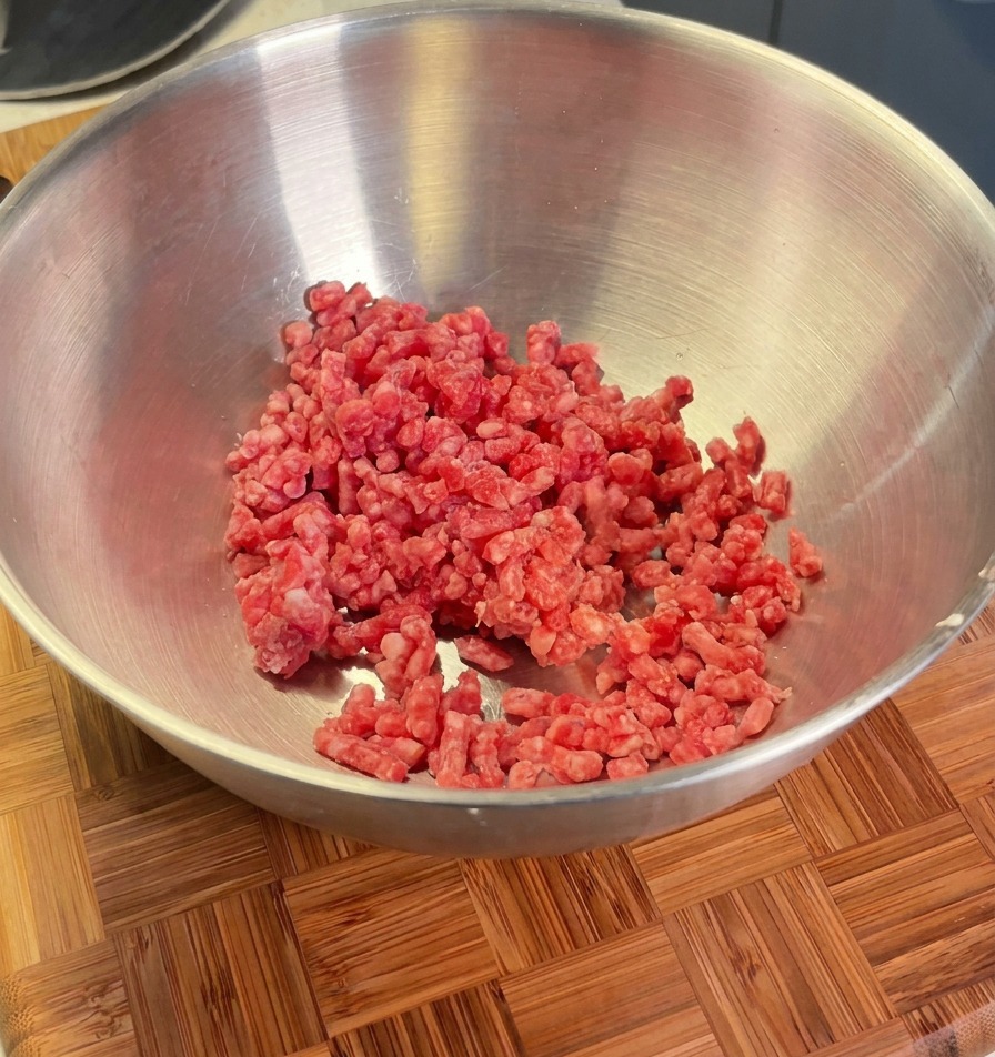 Viande hachée dans un bol en métal prête à être assaisonnée avec des échalotes, du sel et du poivre noir.