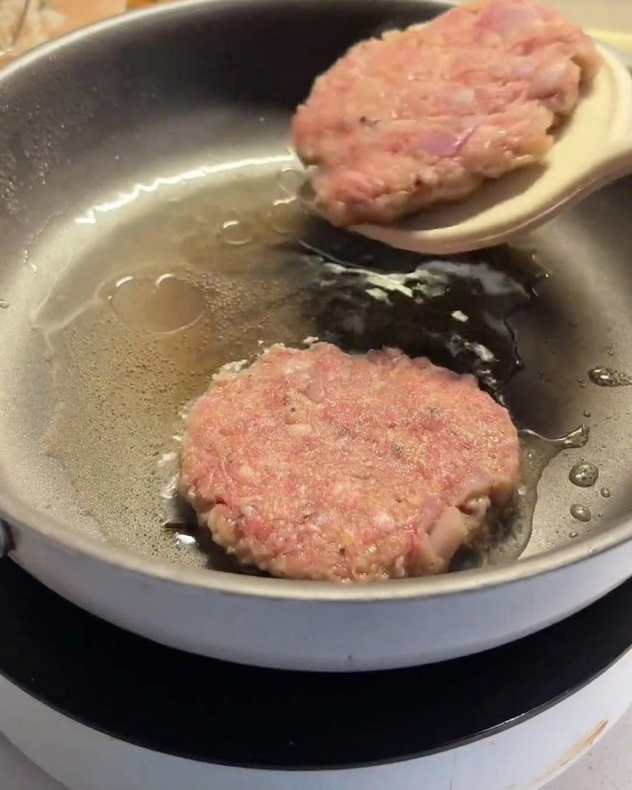 Une spatule retournant un steak haché partiellement cuit dans la poêle.