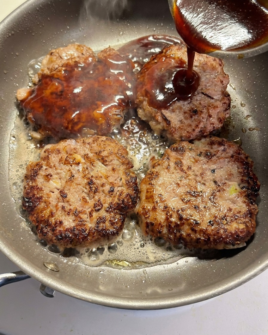 La sauce versée sur quatre steaks de bœuf dorés dans une poêle.