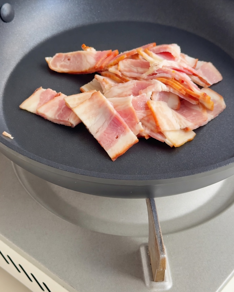Morceaux de bacon en train de dorer dans une poêle.