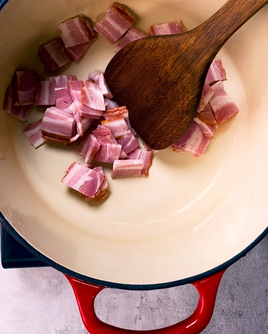 Morceaux de lard dorés et croustillants en train de frire dans une grande cocotte en fonte émaillée.