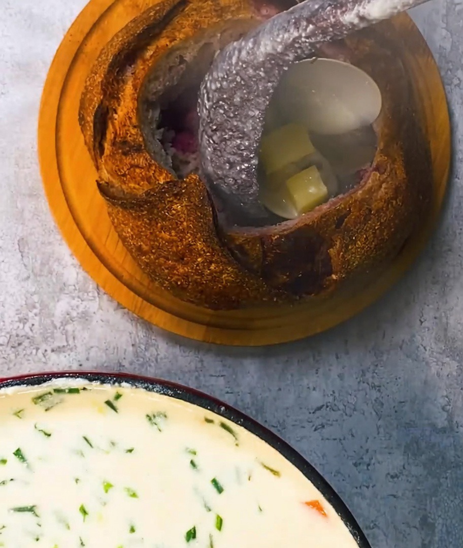 Une riche chaudrée de palourdes crémeuse versée à la louche dans un bol de pain rustique, garnie de morceaux de lard croustillants.