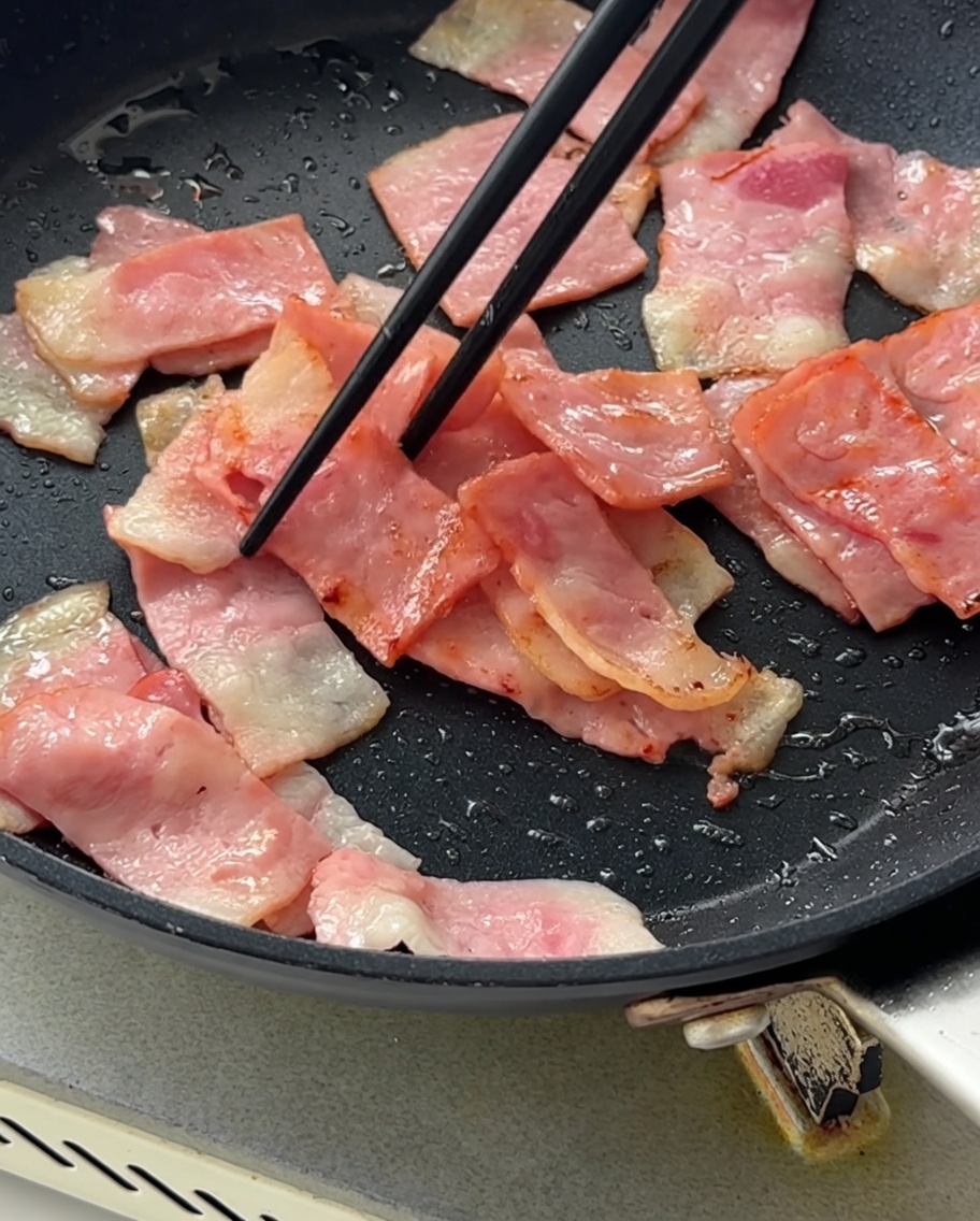 Oignons rouges hachés incorporés dans la poêle avec le bacon doré.