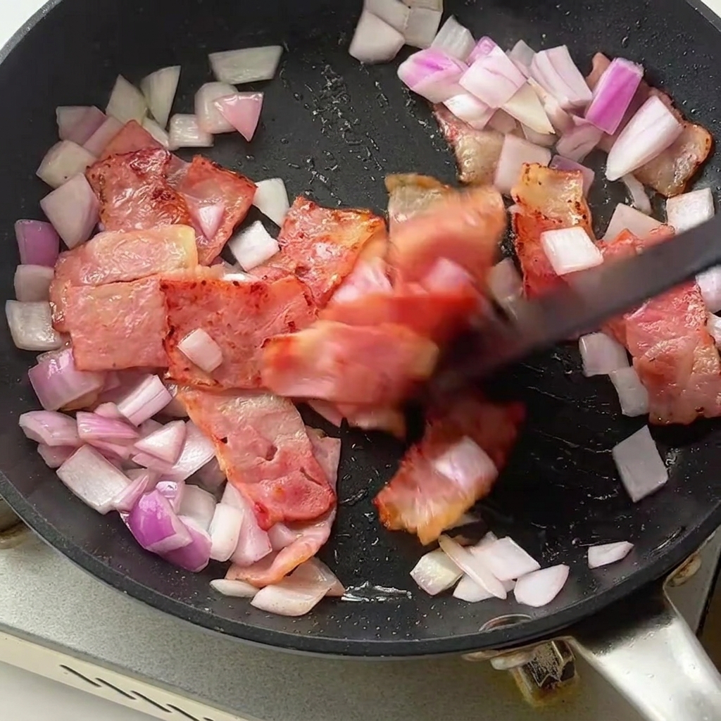 Fusilli et asperges vertes incorporés dans la poêle avec le bacon et les oignons.